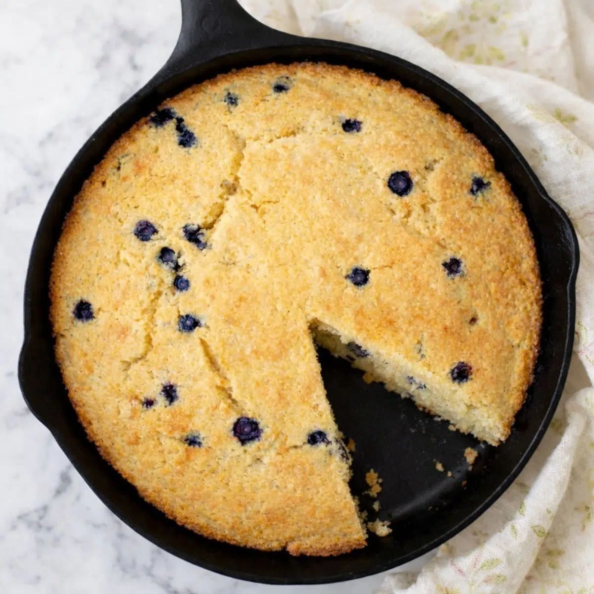 skillet of chickpea flour blueberry bread with a wedge cut out