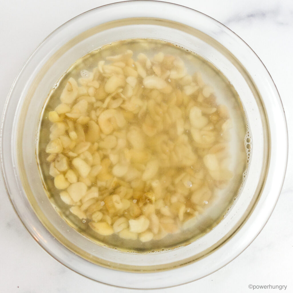 cashews soaking in boiling water, in a clear glass bowl