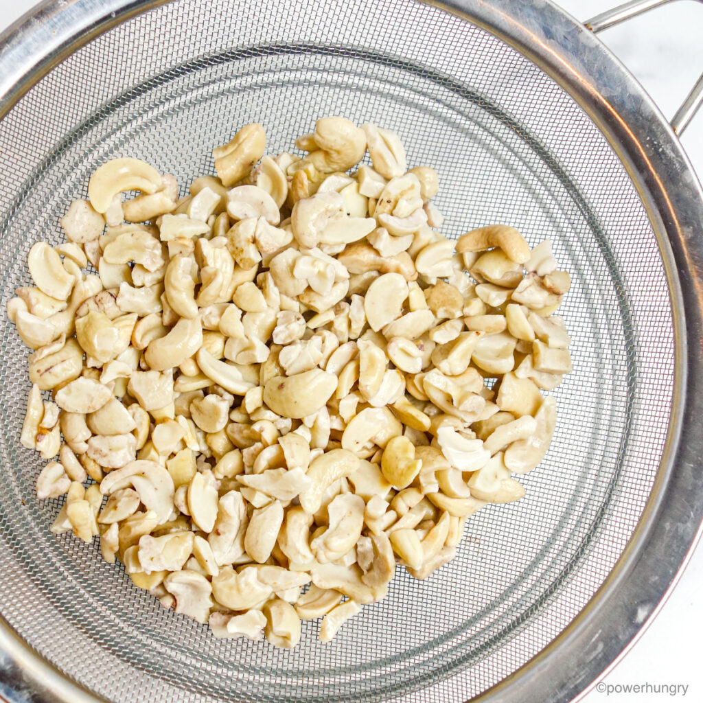 raw, soaked cashews in a silver mesh sieve