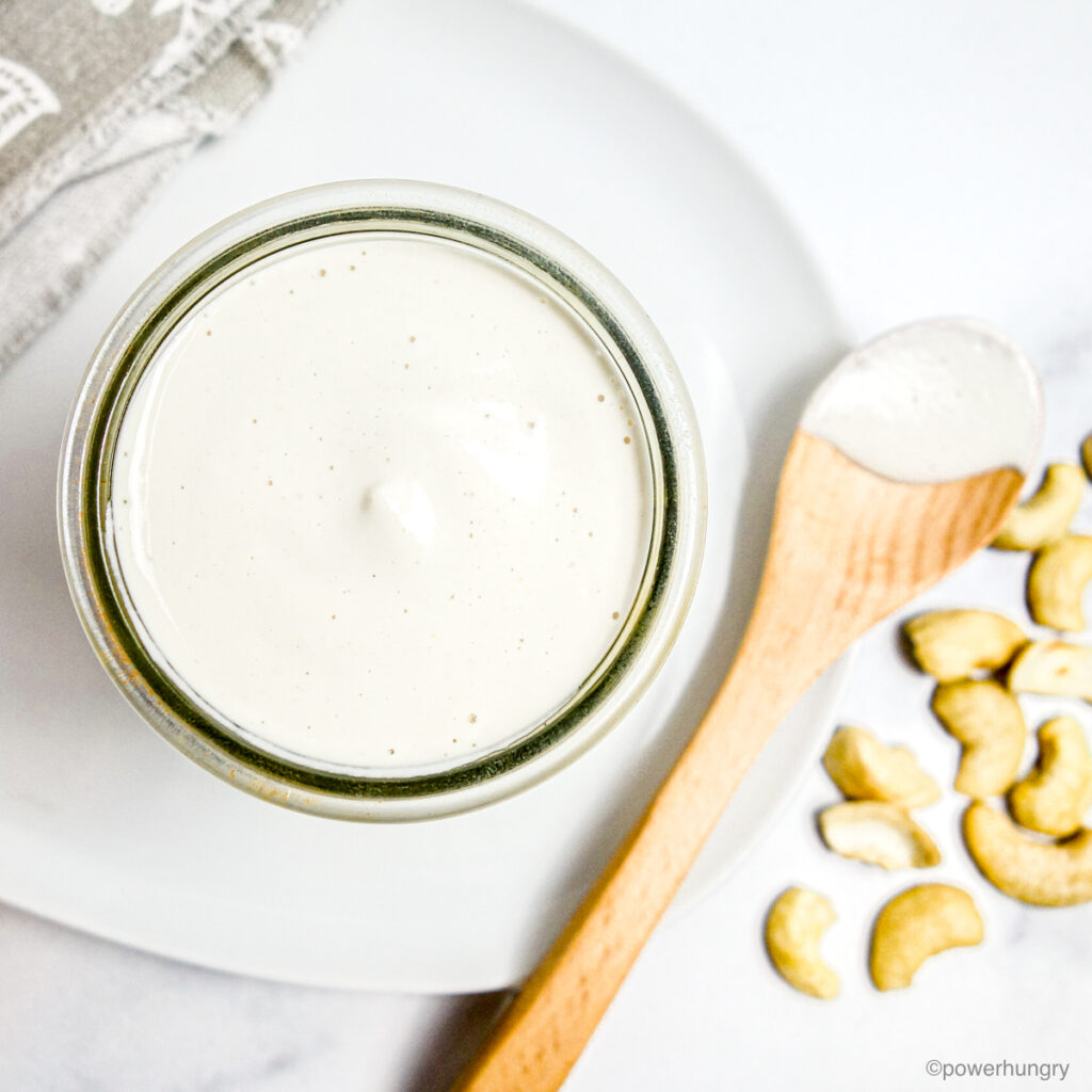 overhead shot of easy 1-ingredient cashew cream in a glass jar atop a white plate