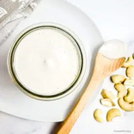 overhead shot of easy 1-ingredient cashew cream in a glass jar atop a white plate