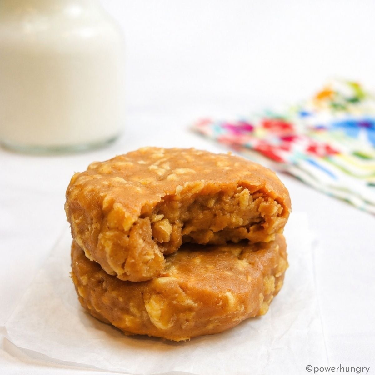 Two 3-ingredient no bake protein cookies, stacked, with a bite out of one of them.