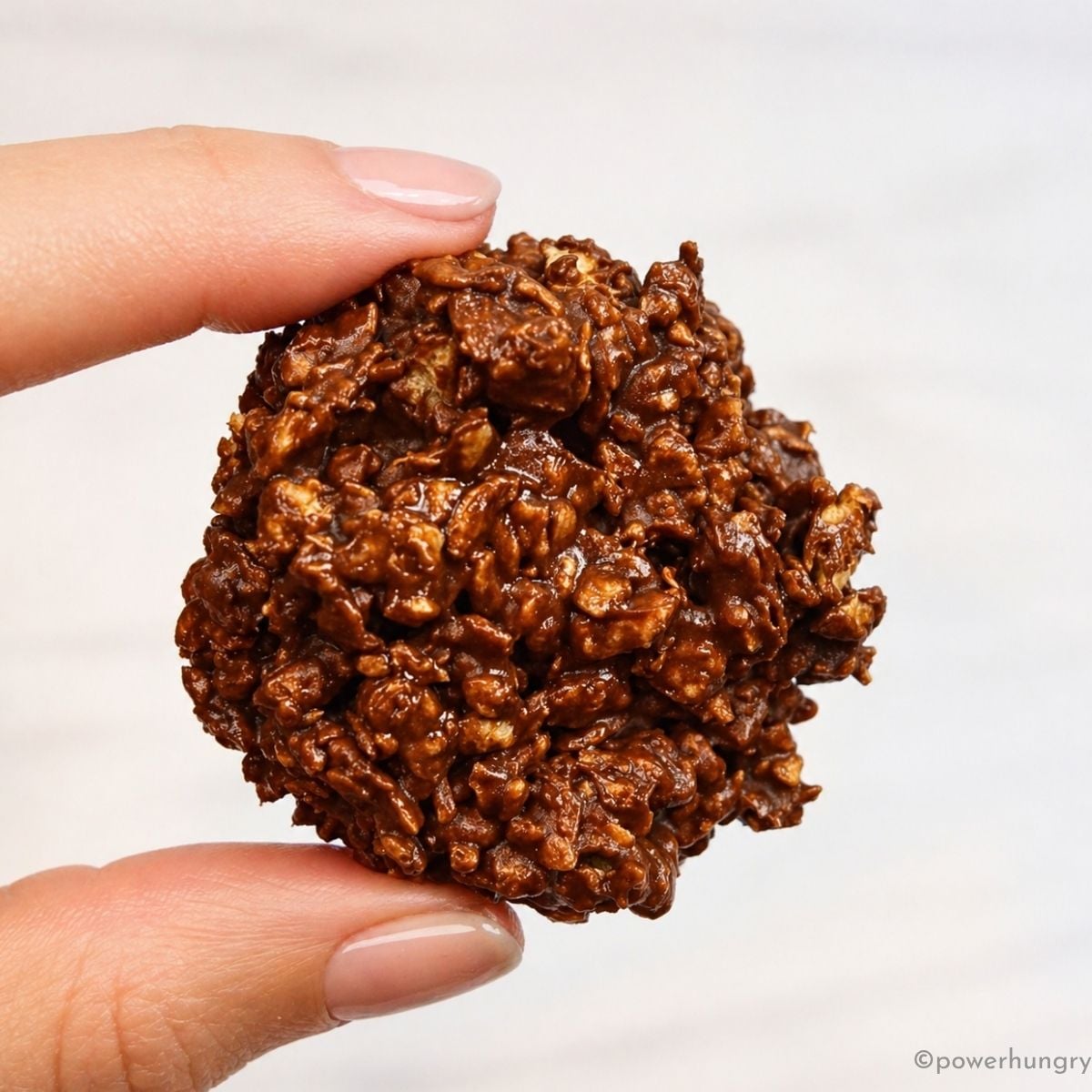 a single 3 ingredient chocolate no-bake protein cookie, held in fingertips